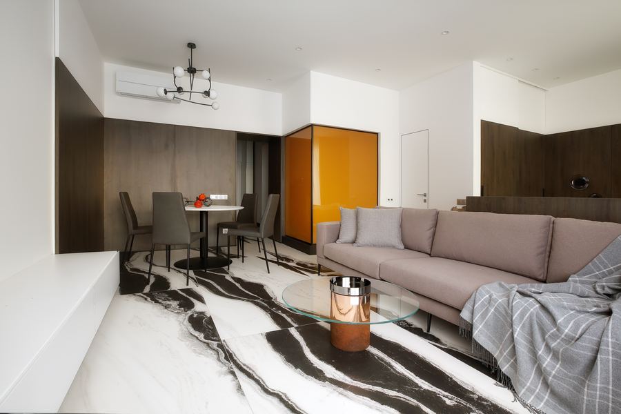 Living and dining area of the Amber Framed in Black and White studio apartment, with amber wardrobe doors and marble patterned flooring.