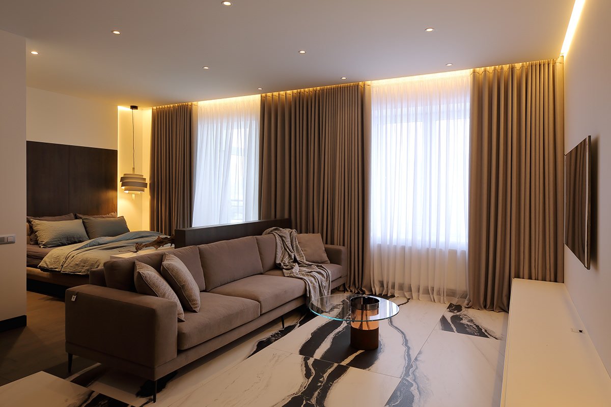 Combined living and sleeping area with sofa and curtains.